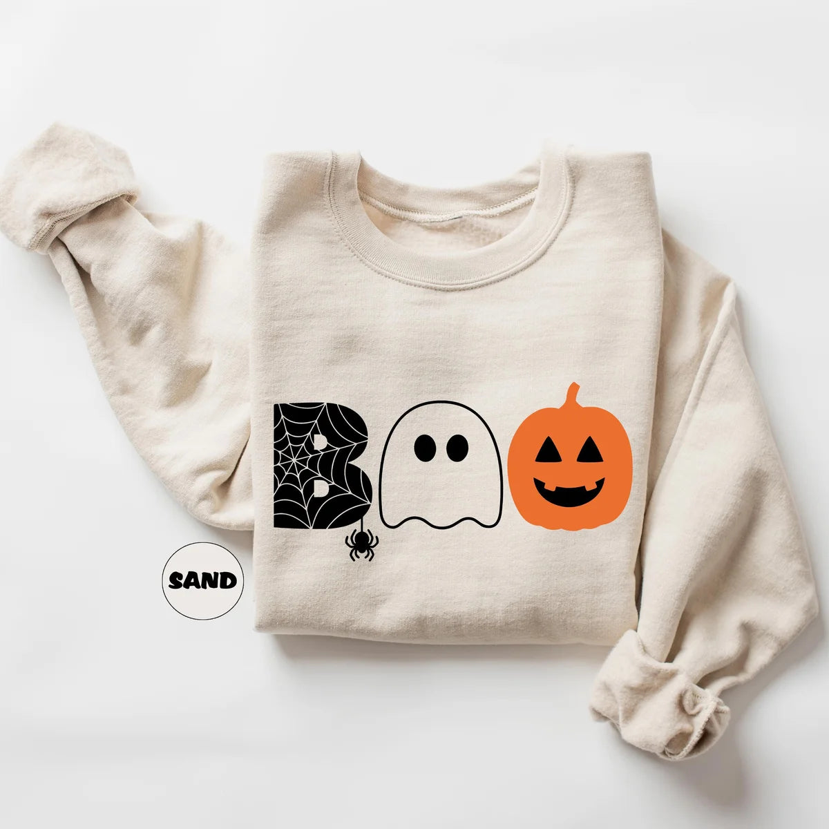 Sand crewneck sweatshirt with the word boo spelled with a spider web letter, a ghost and a jack-o-lantern, flat lay view.