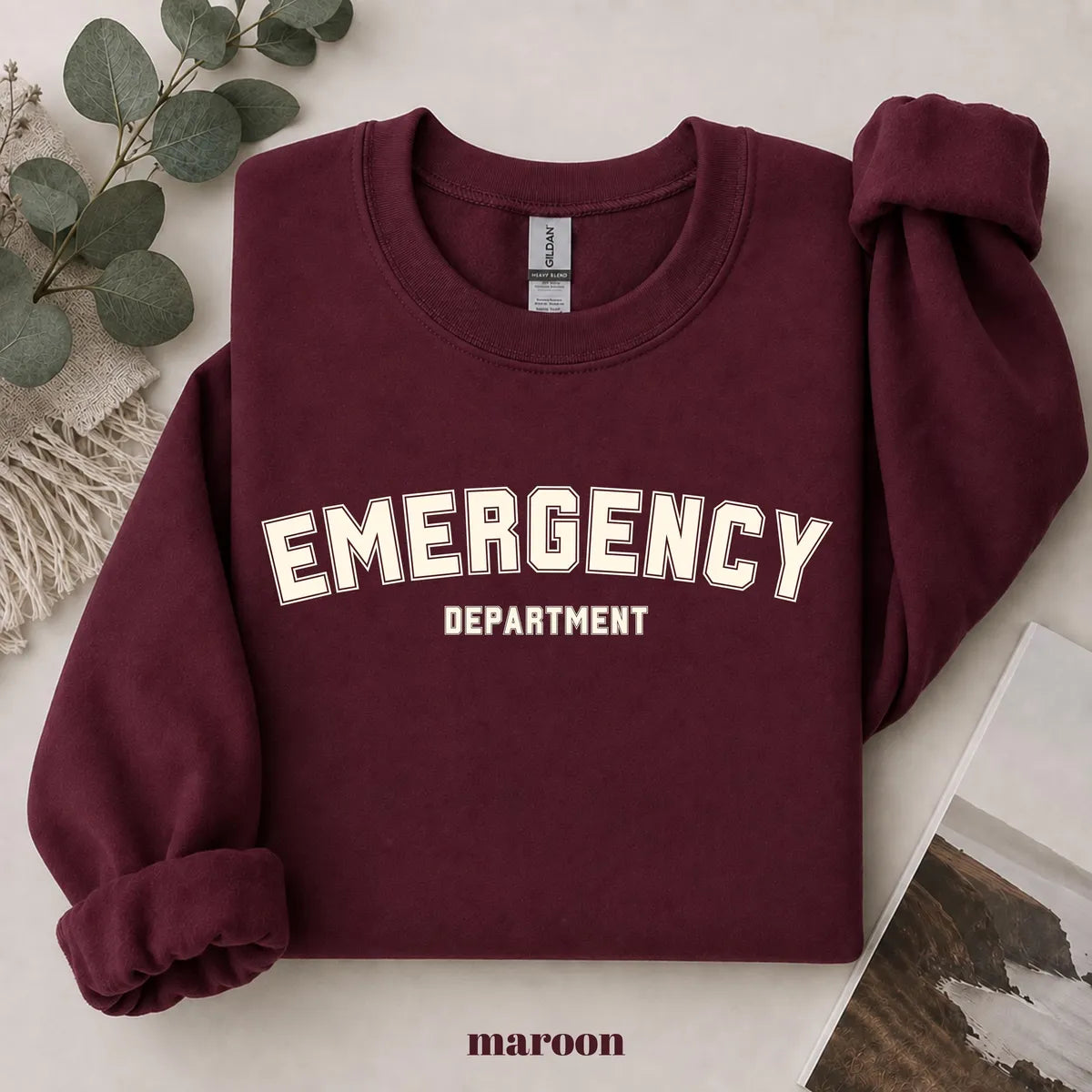 Maroon crewneck sweatshirt with printed varsity style emergency department lettering, flat lay view.