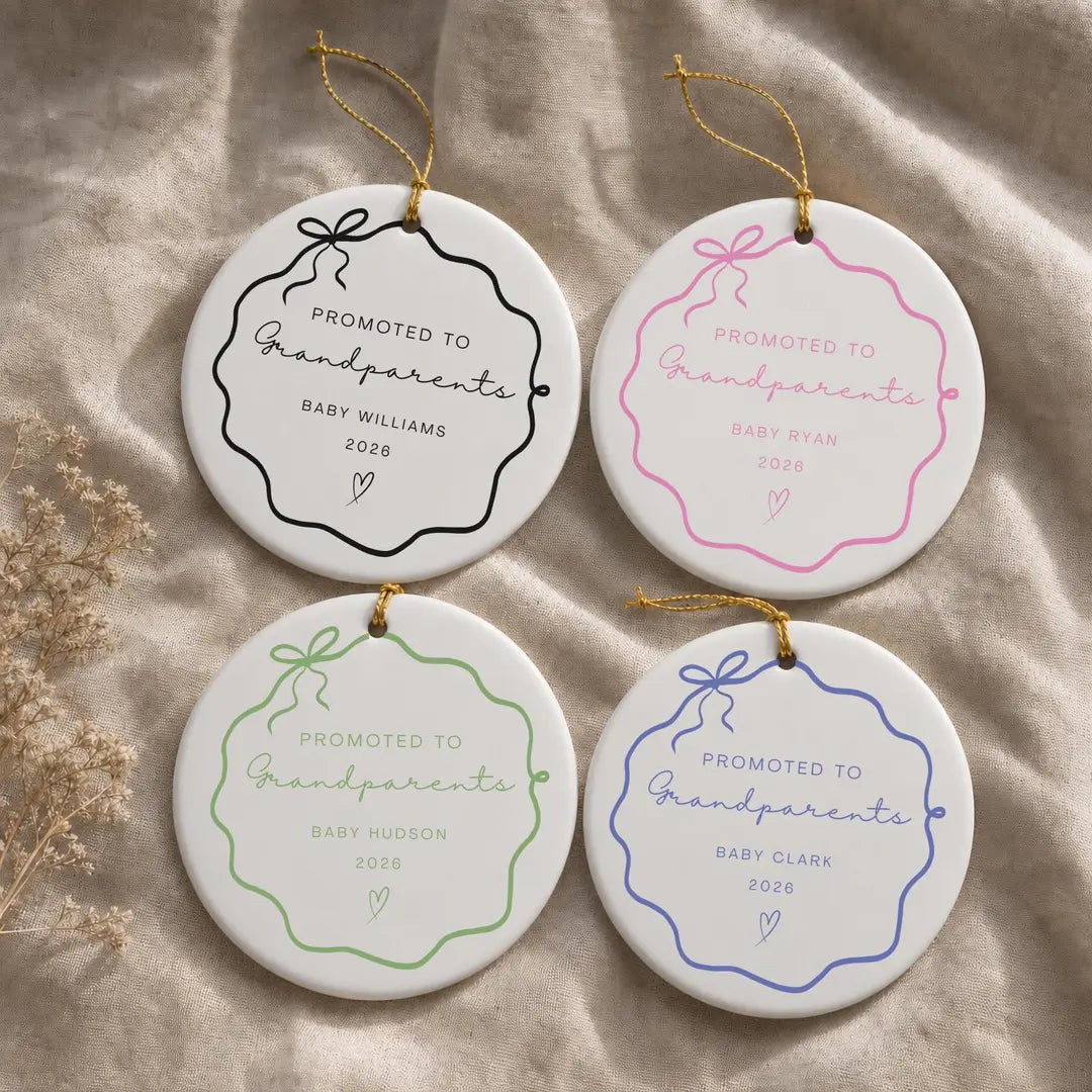 Four round white ceramic Promoted to Grandparents ornaments with wavy bow frames in black, pink, green, and blue and a personalized baby name and year