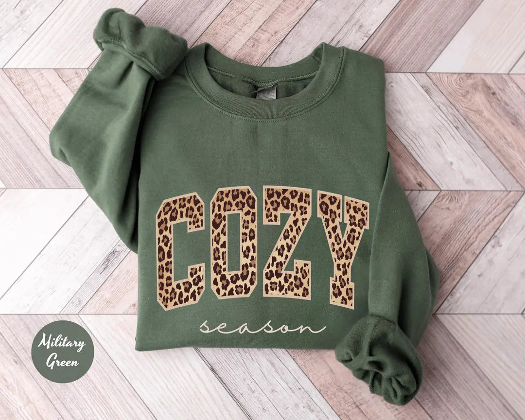 Military Green crewneck sweatshirt with bold leopard print cozy lettering above the script words season, flat lay view.