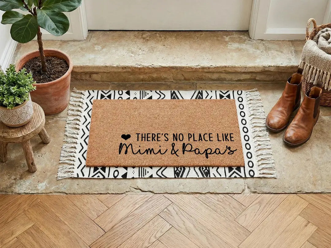 Coir doormat with a There's No Place Like Mimi and Papa's message layered on a black and white fringed rug with leather boots on a herringbone floor
