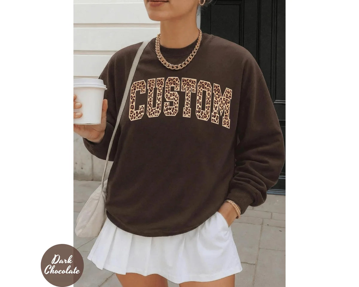 Dark Chocolate crewneck sweatshirt with bold leopard print varsity lettering with your own custom name or text, worn by a model.