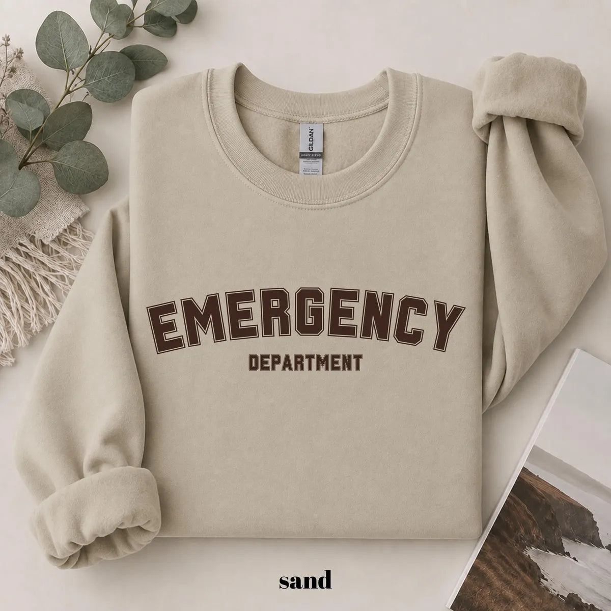 Sand crewneck sweatshirt with printed varsity style emergency department lettering, flat lay view.