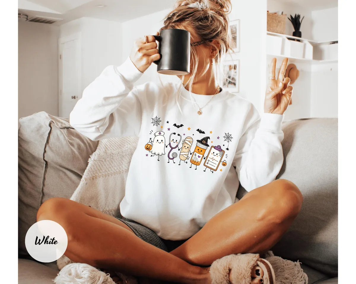 White crewneck sweatshirt with a ghost, stethoscope, bandage and medical chart characters with Halloween details, worn by a model.