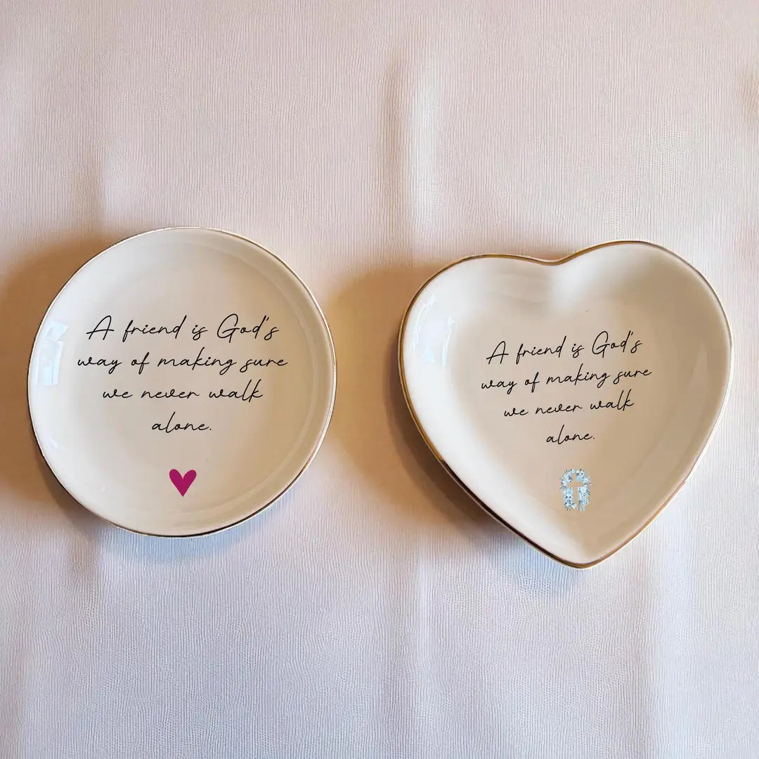 Round ceramic ring dish with a small pink heart beside a heart-shaped dish with a blue floral cross, both with the same quote