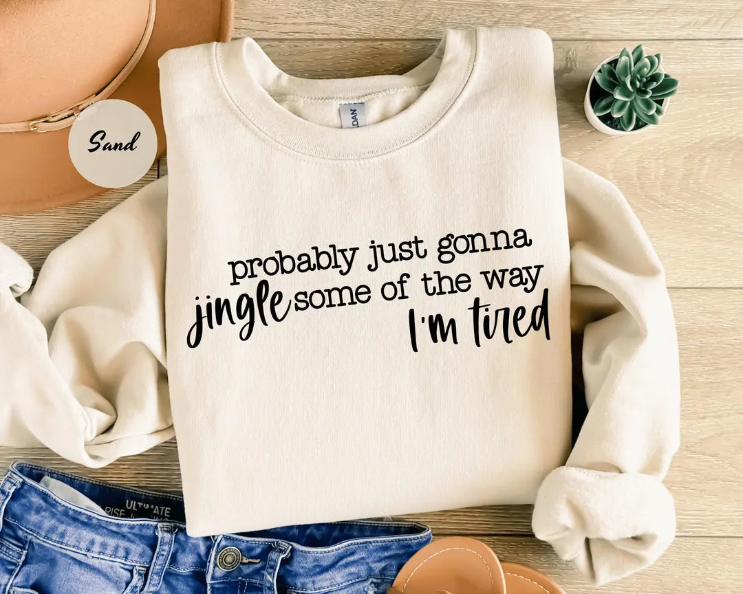 Sand crewneck sweatshirt with script lettering that reads probably just gonna jingle some of the way I'm tired, flat lay view.
