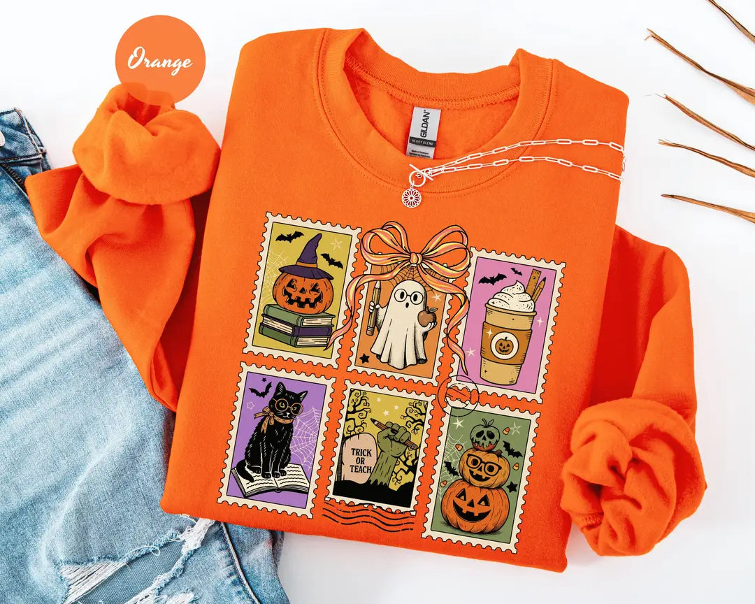 Orange crewneck sweatshirt with six vintage postage-style stamps with a ghost, black cat, pumpkins and a coffee cup, flat lay view.