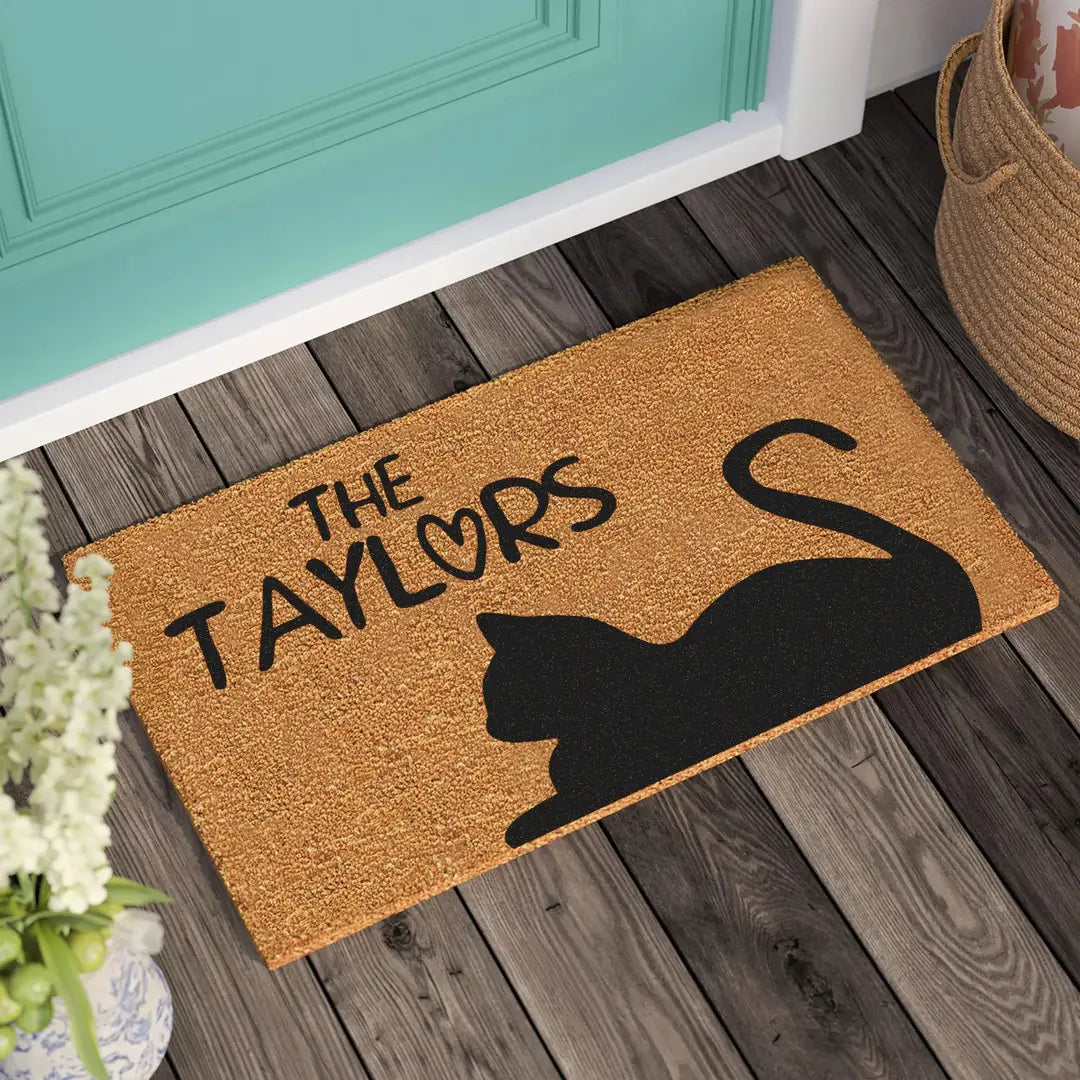 Rectangular coir doormat with a black cat silhouette and family name in front of a teal door