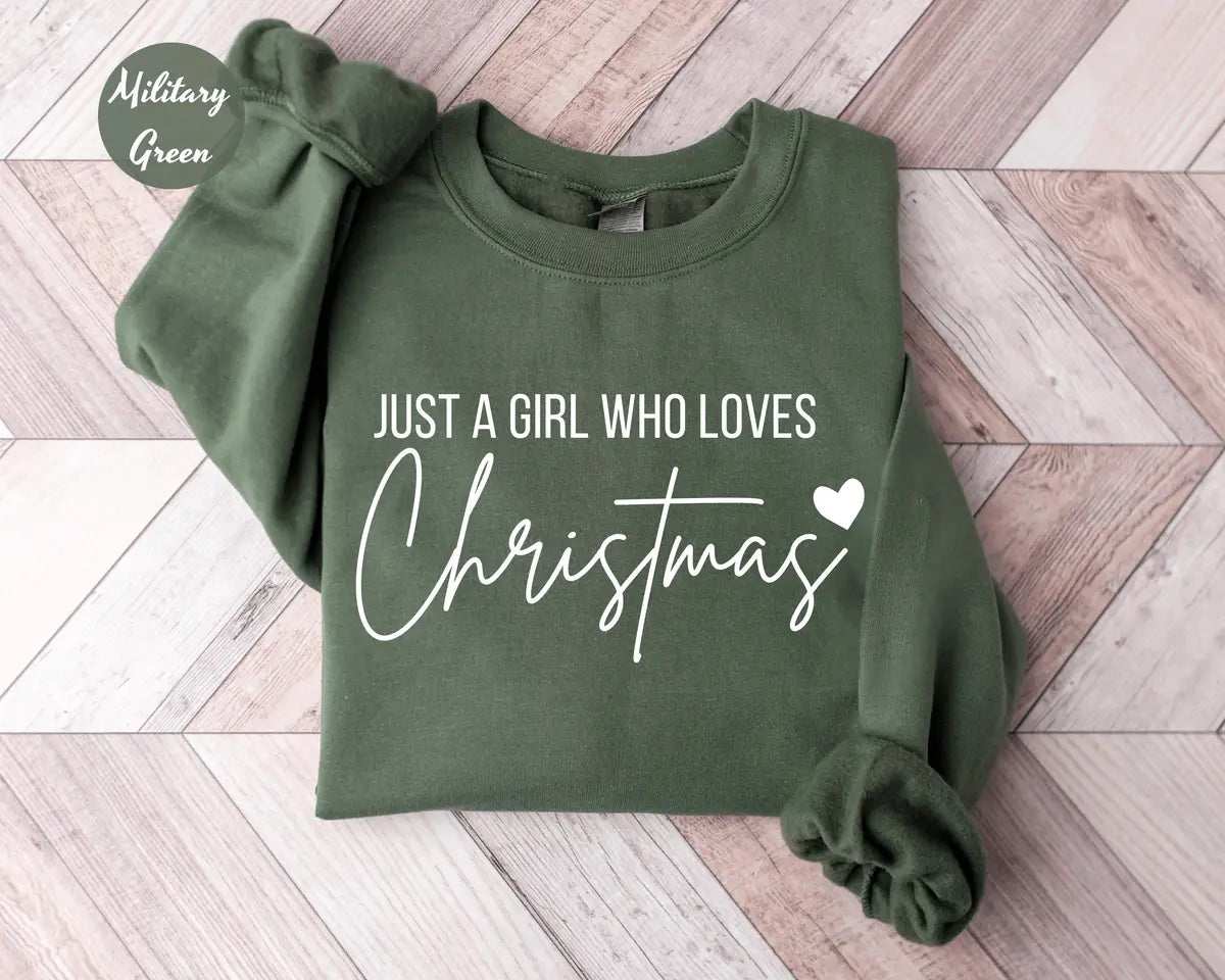 Military Green crewneck sweatshirt with script lettering that reads just a girl who loves Christmas with a small heart, flat lay view.
