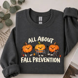 Dark Heather crewneck sweatshirt with printed pumpkins with a walker and wheelchair above the words all about fall prevention, flat lay view.