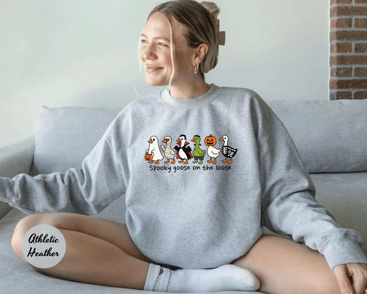 Athletic Heather crewneck sweatshirt with costumed geese dressed as a ghost, vampire, pumpkin and skeleton above the words spooky goose on the loose, worn by a model.