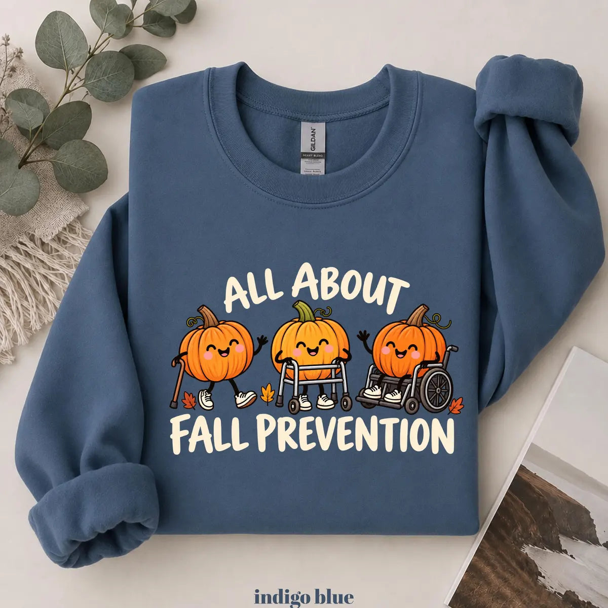 Indigo Blue crewneck sweatshirt with printed pumpkins with a walker and wheelchair above the words all about fall prevention, flat lay view.