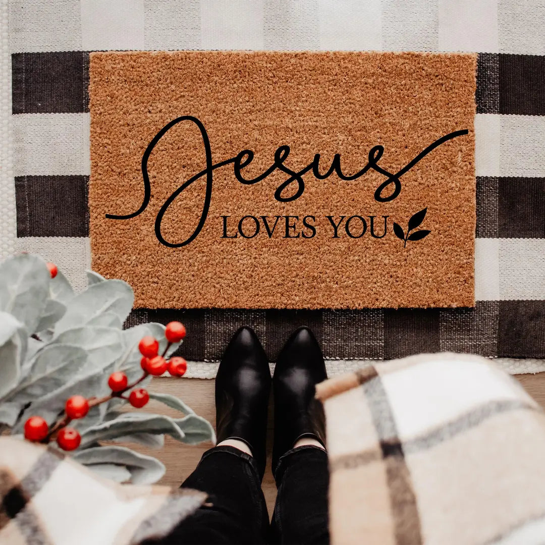 Rectangular coir doormat with Jesus Loves You script lettering on a buffalo check rug with red berries