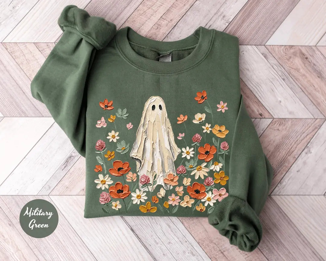 Military Green crewneck sweatshirt with printed a ghost standing in a field of autumn wildflowers, flat lay view.