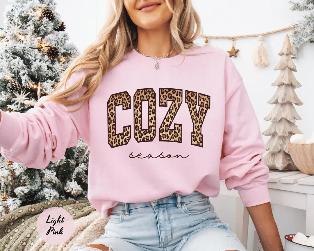 Light Pink crewneck sweatshirt with bold leopard print cozy lettering above the script words season, worn by a model.