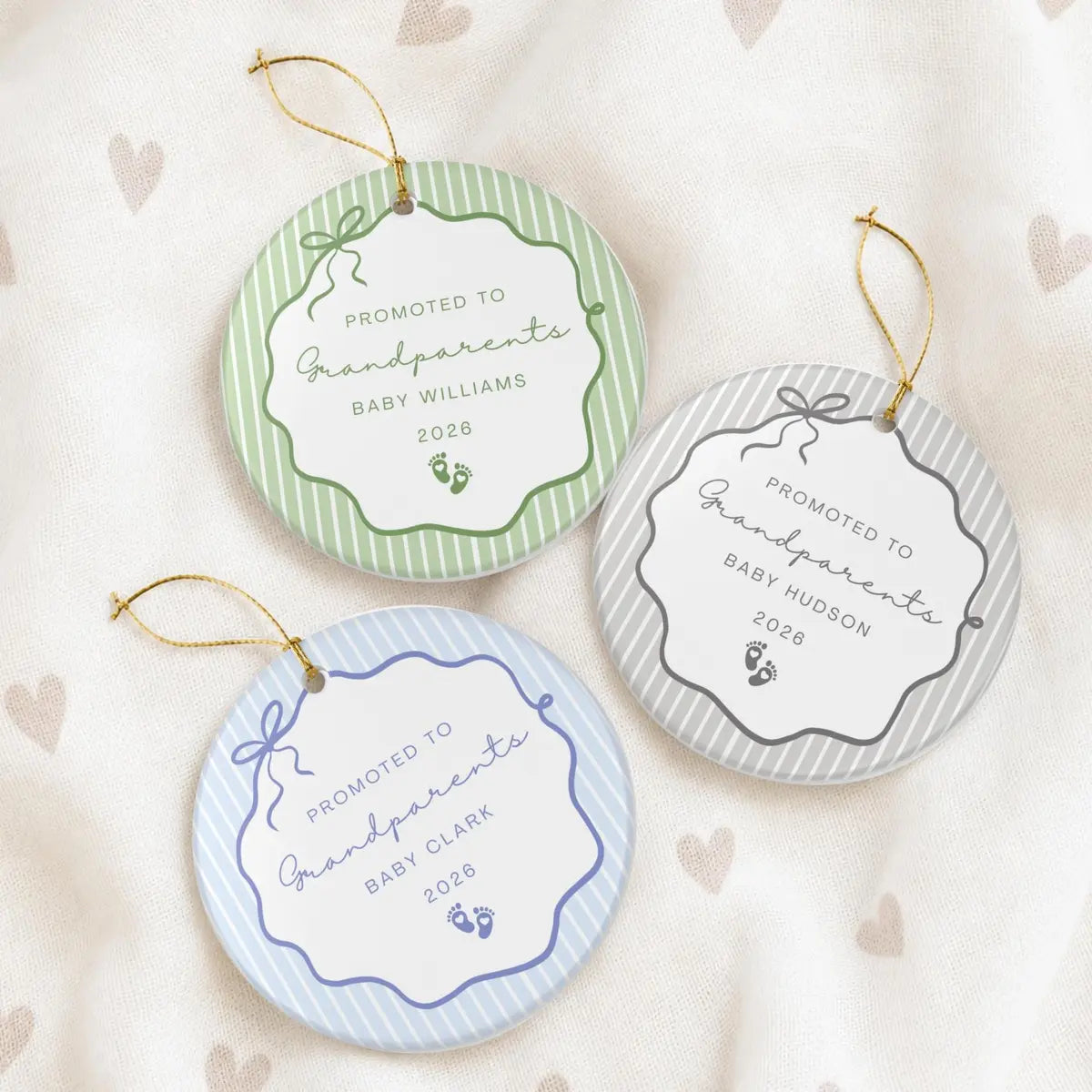 Green, gray, and blue pinstripe round ceramic Promoted to Grandparents ornaments with baby footprints on a cream heart-print fabric