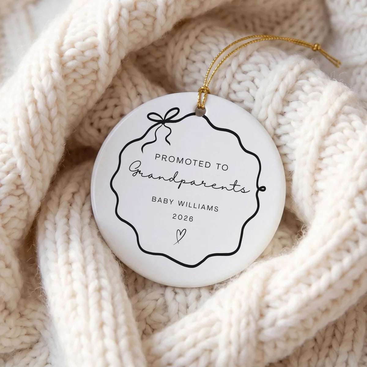 Black wavy bow frame round ceramic Promoted to Grandparents ornament with a personalized name and year on a cream knit sweater