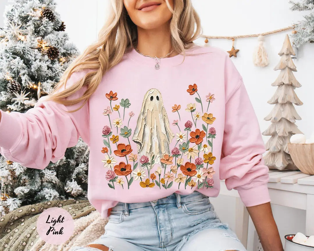 Light Pink crewneck sweatshirt with printed a ghost standing in a field of autumn wildflowers, worn by a model.