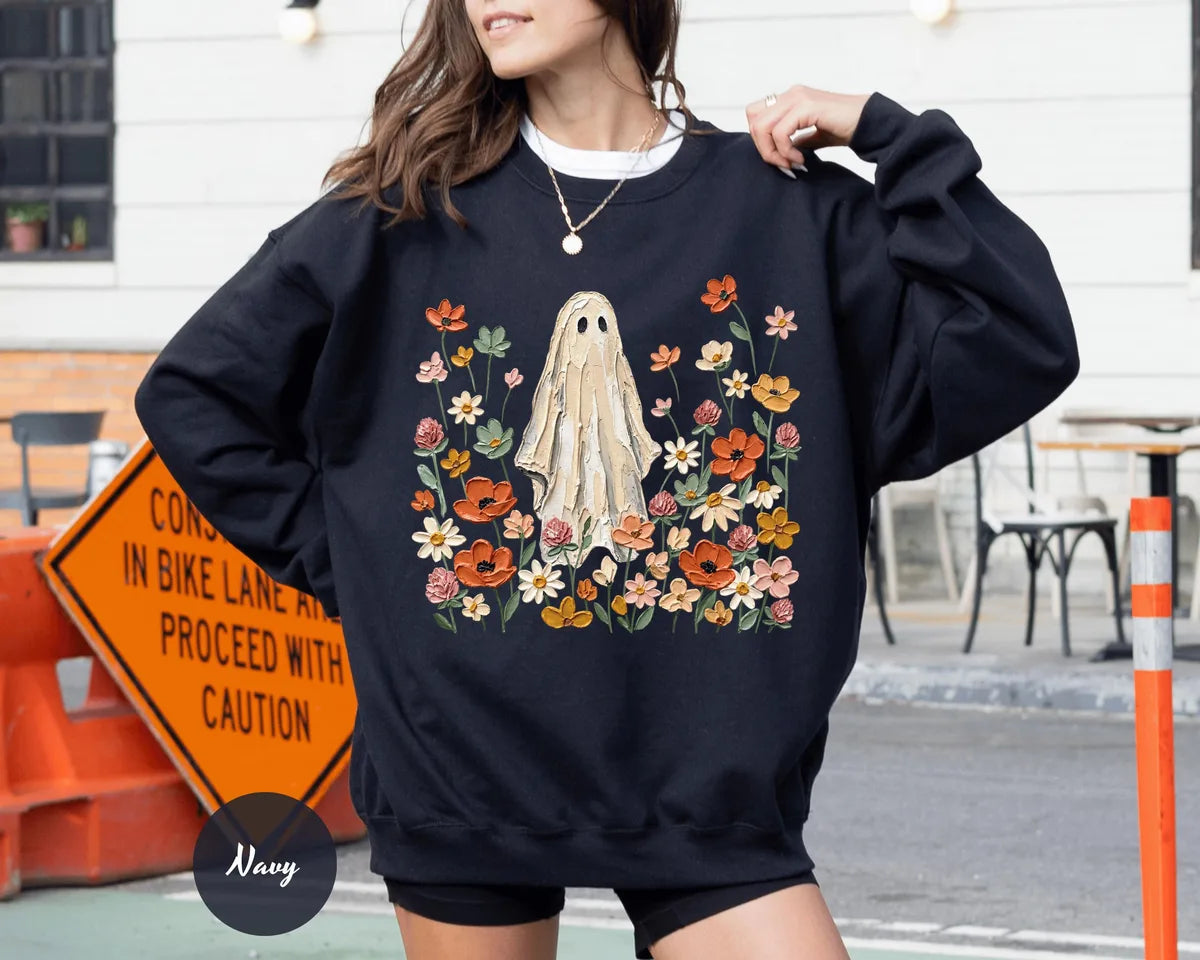 Navy crewneck sweatshirt with printed a ghost standing in a field of autumn wildflowers, worn by a model.