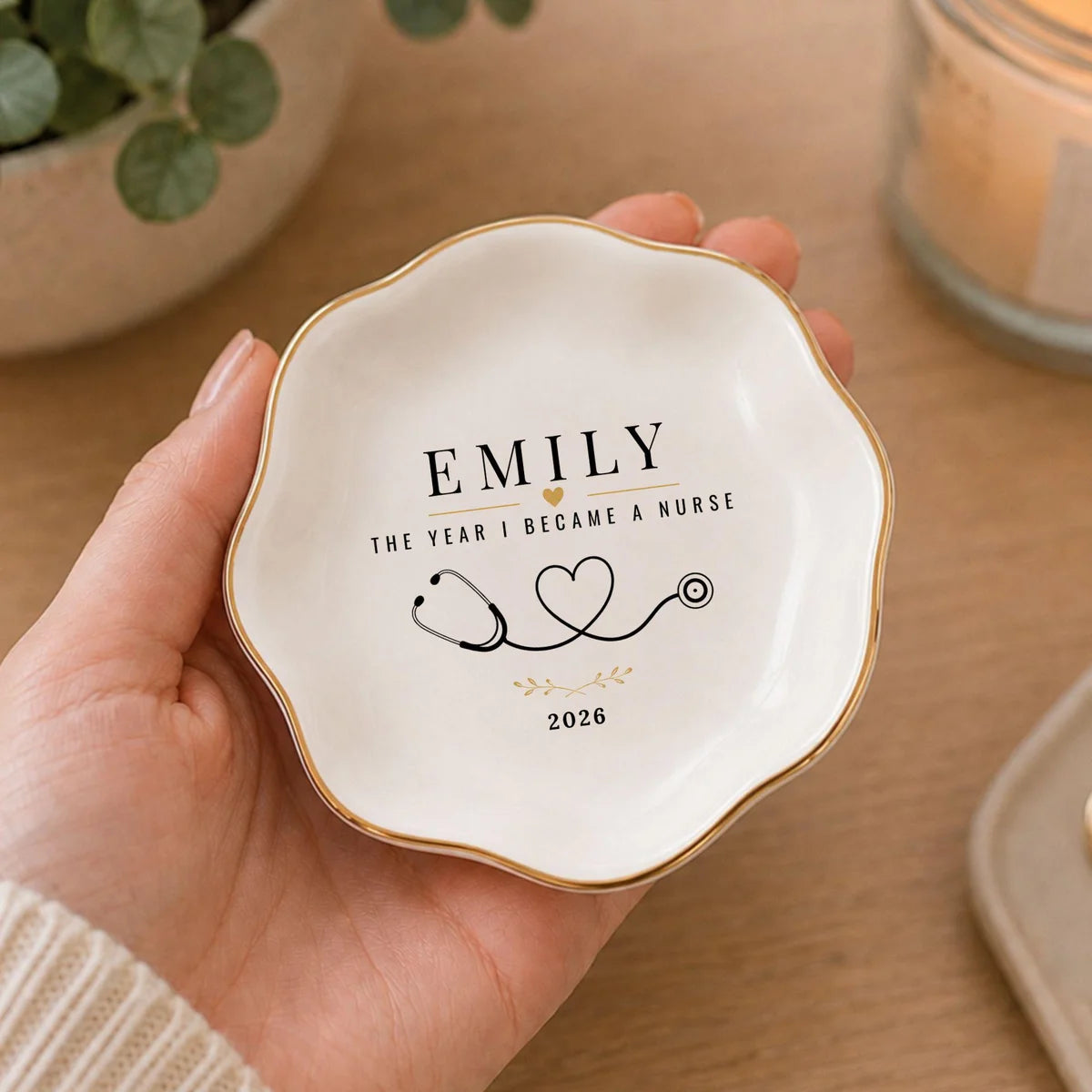 Hand holding a wavy round ceramic nurse ring dish with a name, stethoscope heart design and a year