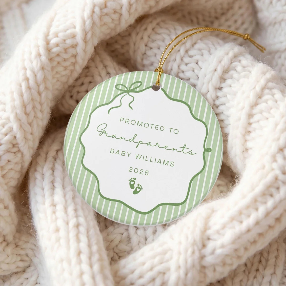 Green pinstripe round ceramic Promoted to Grandparents ornament with baby footprints and a personalized name and year on a cream knit blanket