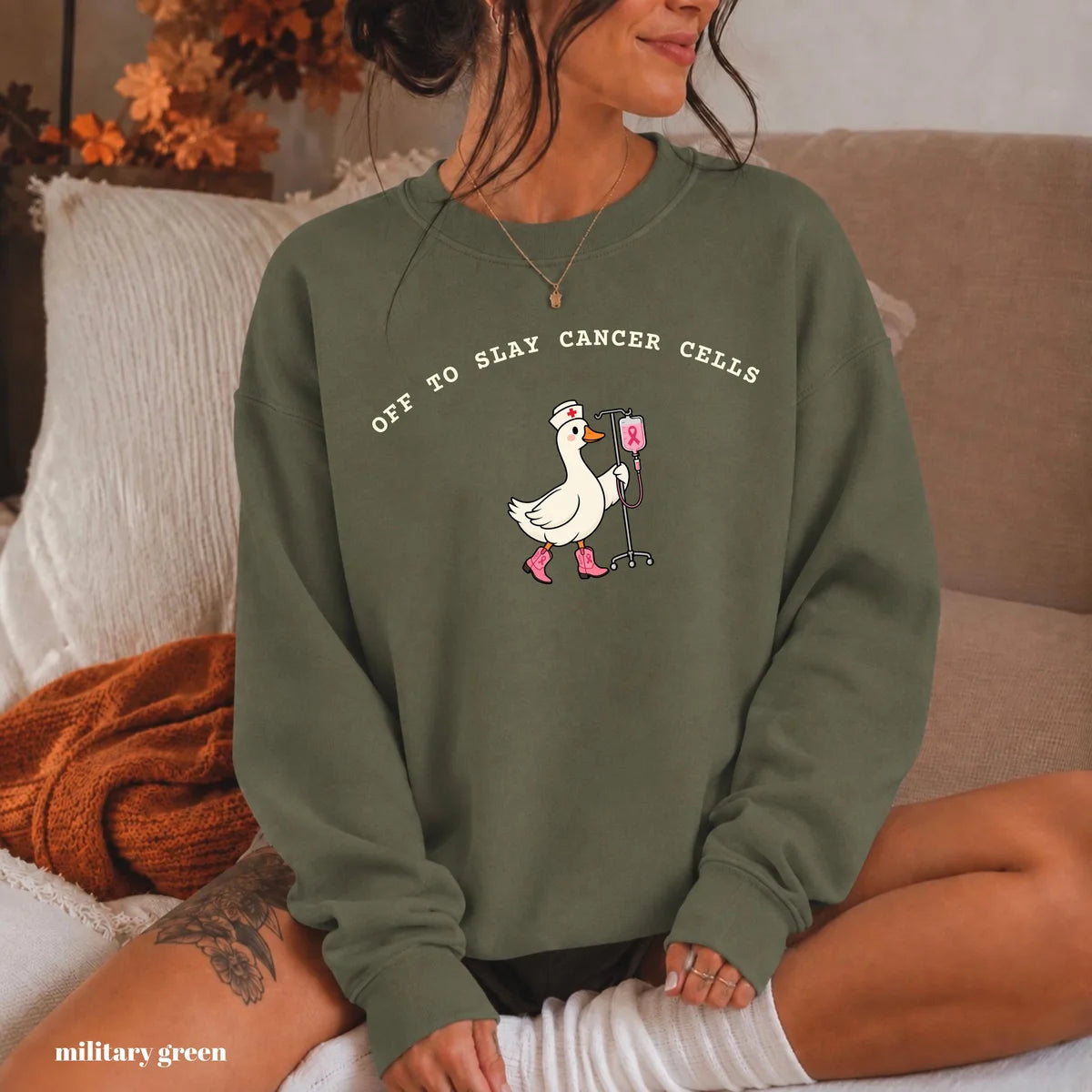 Military Green crewneck sweatshirt with printed a nurse goose in pink boots with an IV pole and the words off to slay cancer cells, worn by a model.