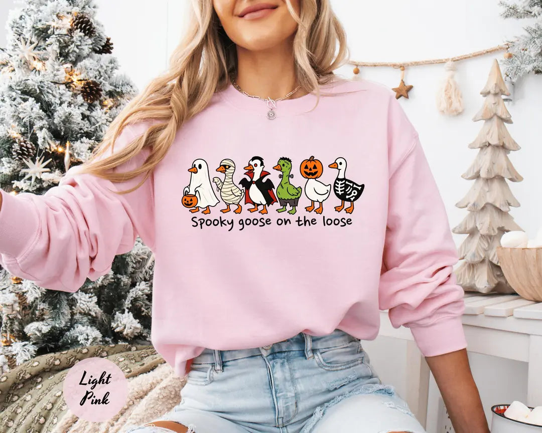 Light Pink crewneck sweatshirt with costumed geese dressed as a ghost, vampire, pumpkin and skeleton above the words spooky goose on the loose, worn by a model.