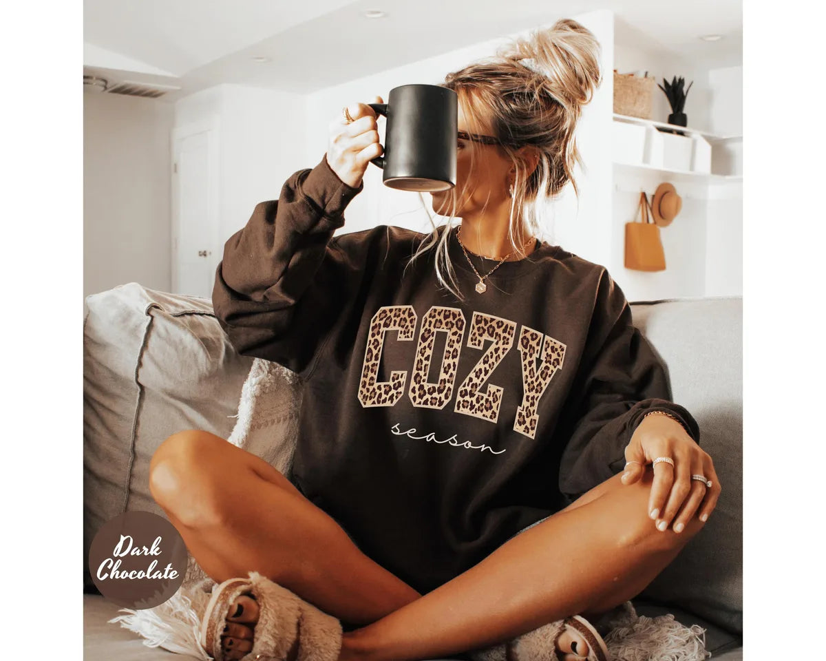 Dark Chocolate crewneck sweatshirt with bold leopard print cozy lettering above the script words season, worn by a model.