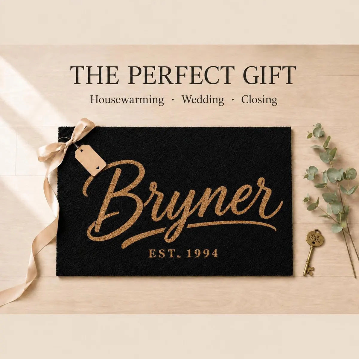 Black doormat with a gold-tone script surname and established year styled as a gift with ribbon, tag, and key