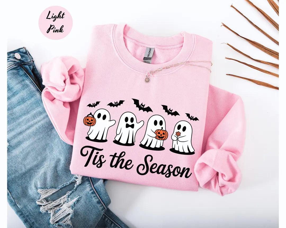 Light Pink crewneck sweatshirt with printed four cute ghosts with pumpkins and bats above the words tis the season, flat lay view.