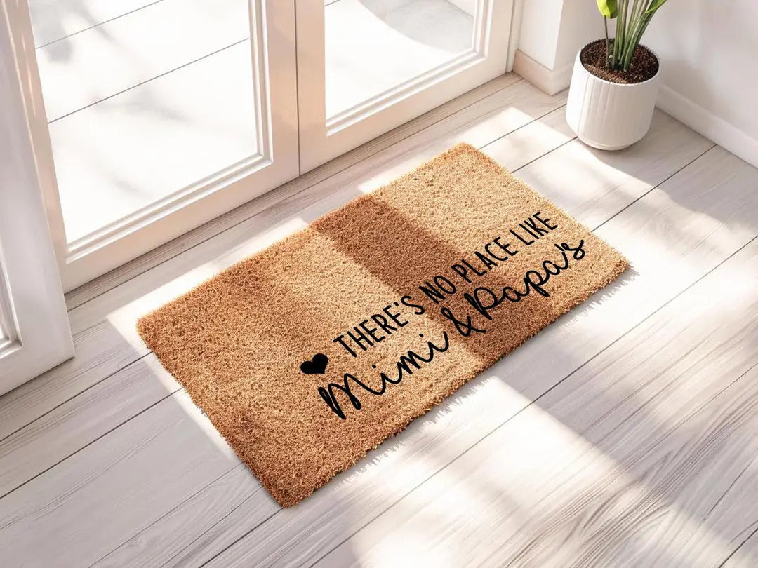 Coir doormat with a There's No Place Like Mimi and Papa's message in sunlight beside a glass door and a potted plant