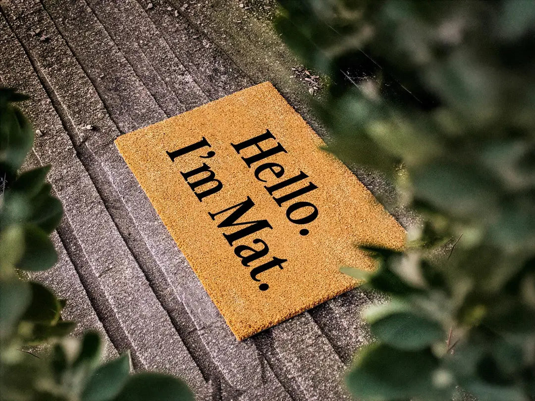 Coir doormat with a Hello I'm Mat message on weathered gray planks with leafy branches
