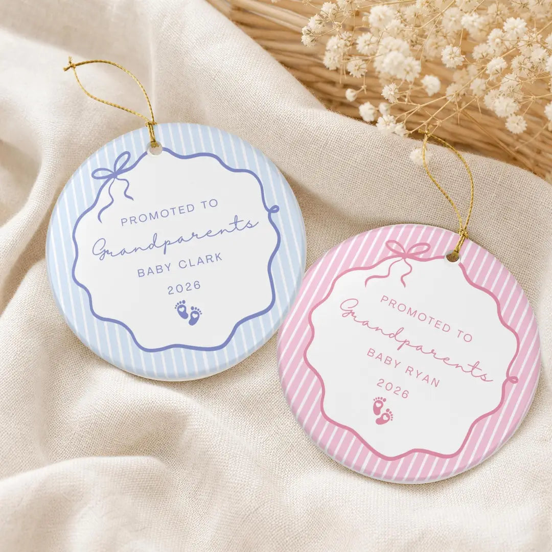 Blue and pink pinstripe round ceramic Promoted to Grandparents ornaments with baby footprints and a personalized name and year on cream fabric