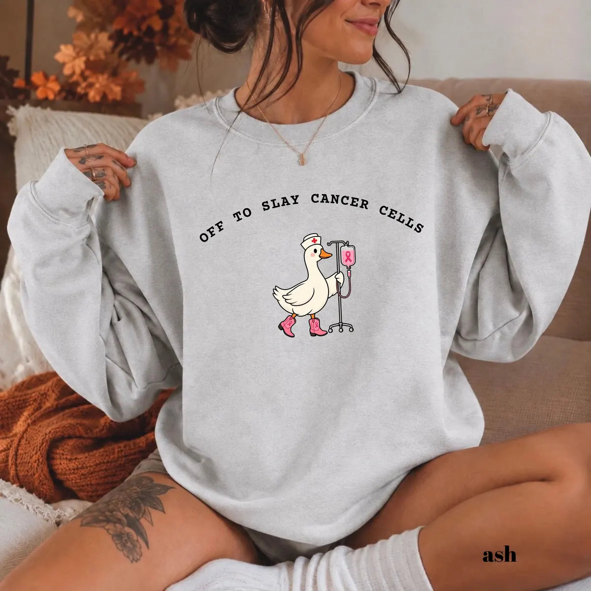 Ash crewneck sweatshirt with printed a nurse goose in pink boots with an IV pole and the words off to slay cancer cells, worn by a model.