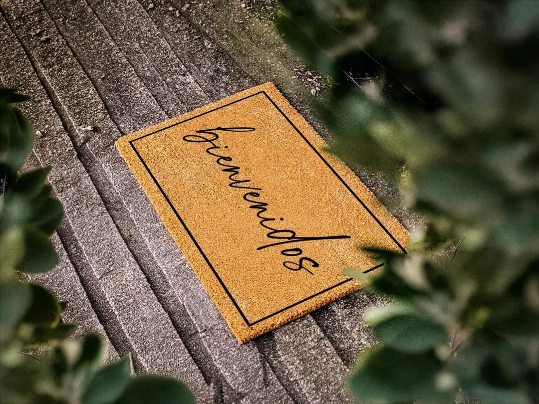 Coir doormat with a framed bienvenidos script message on weathered gray planks with leafy branches