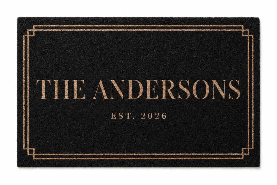 Flat view of a black faux coir doormat with a double gold-tone border, family name, and established year