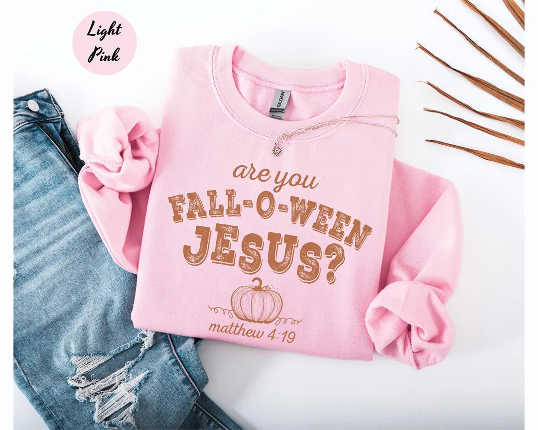Light Pink crewneck sweatshirt with printed a pumpkin with the words are you fall-o-ween jesus and matthew 4:19 in a western style font, flat lay view.