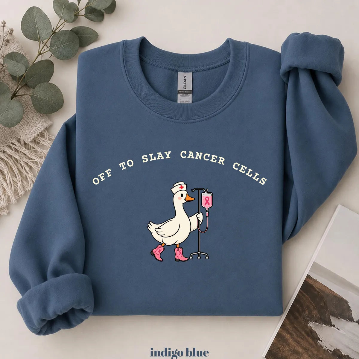 Indigo Blue crewneck sweatshirt with printed a nurse goose in pink boots with an IV pole and the words off to slay cancer cells, flat lay view.