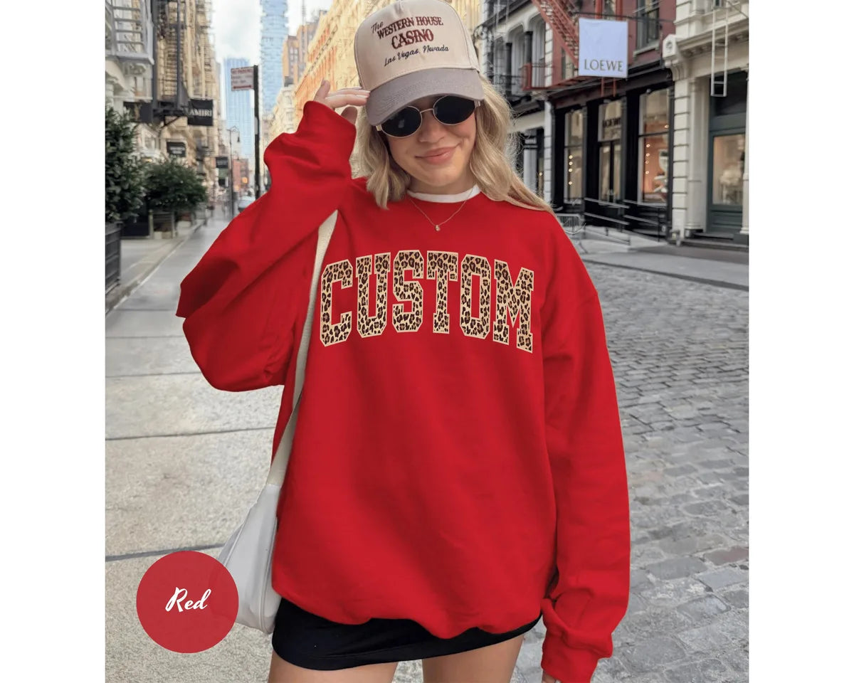 Red GD crewneck sweatshirt with bold leopard print varsity lettering with your own custom name or text, worn by a model.