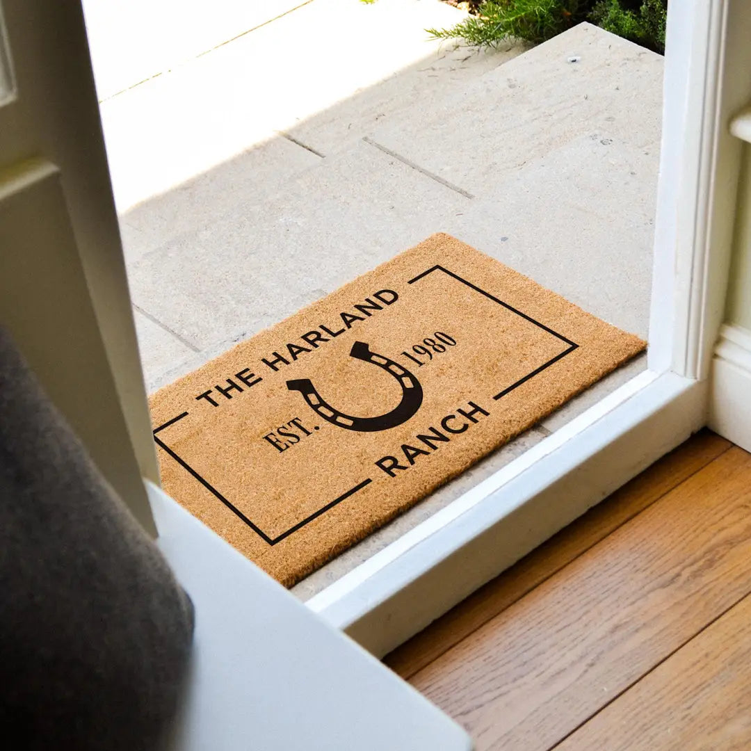 Coir doormat with a horseshoe ranch design on a stone threshold at an open white door