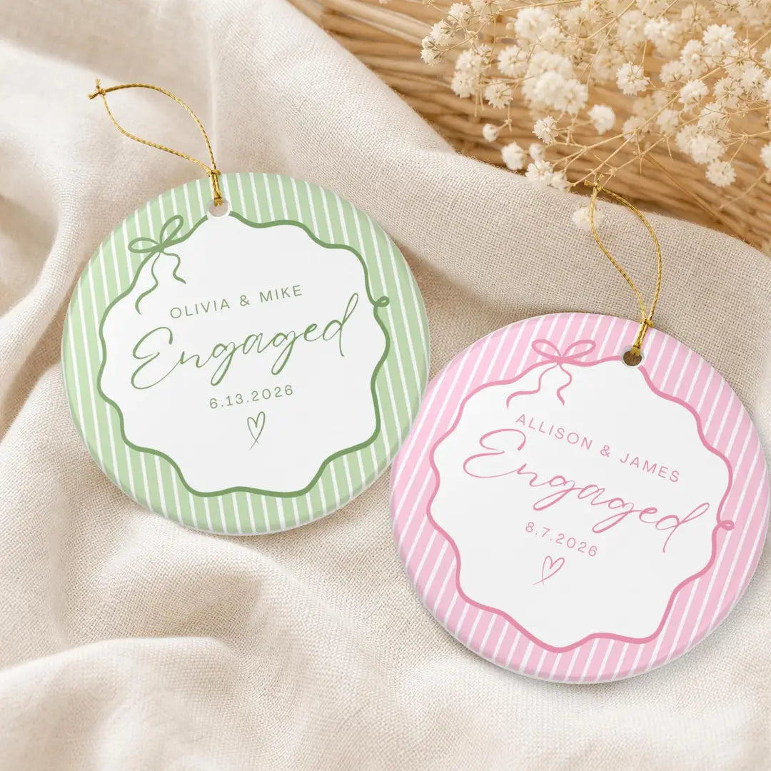 Round white ceramic Engaged ornaments with green and pink pinstripe bow frames and personalized names and date on a cream cloth