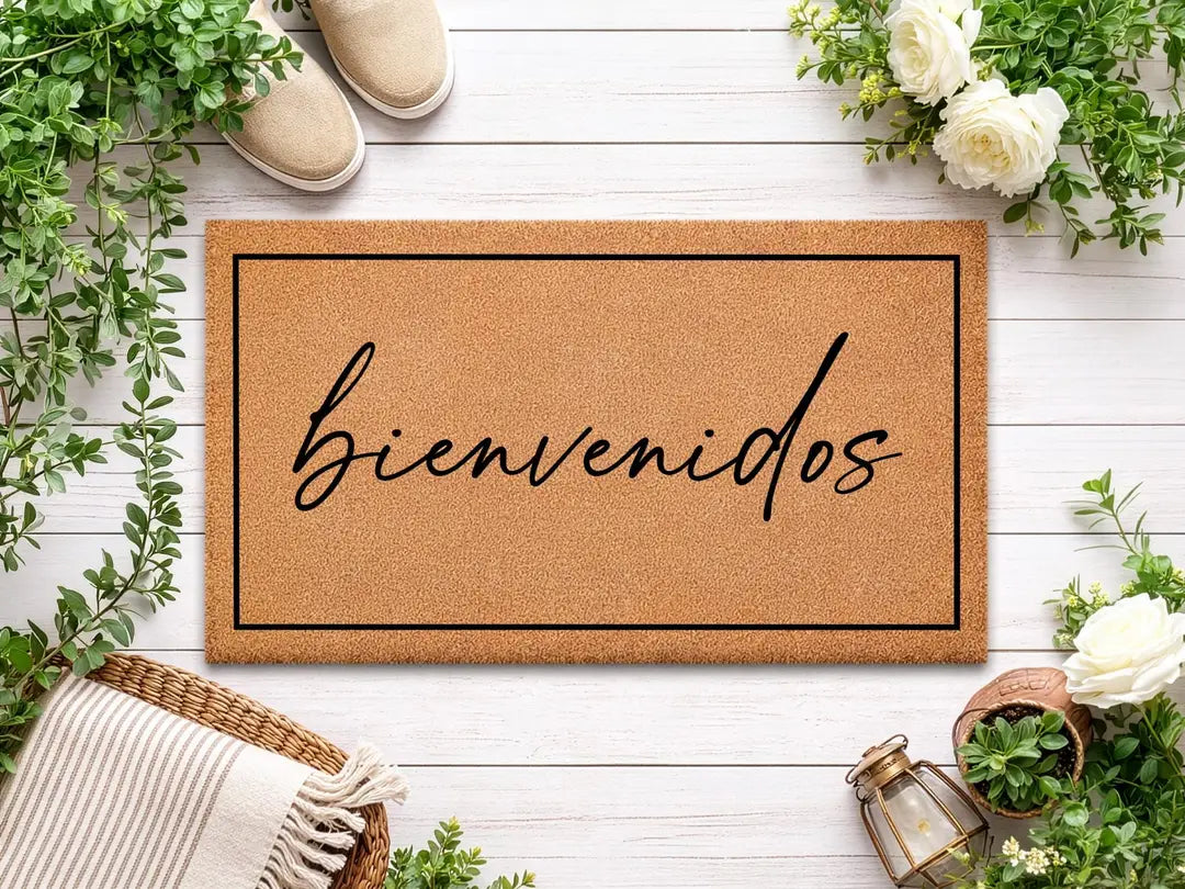Coir doormat with a framed bienvenidos script message on white wood boards with greenery, white roses, and a woven basket
