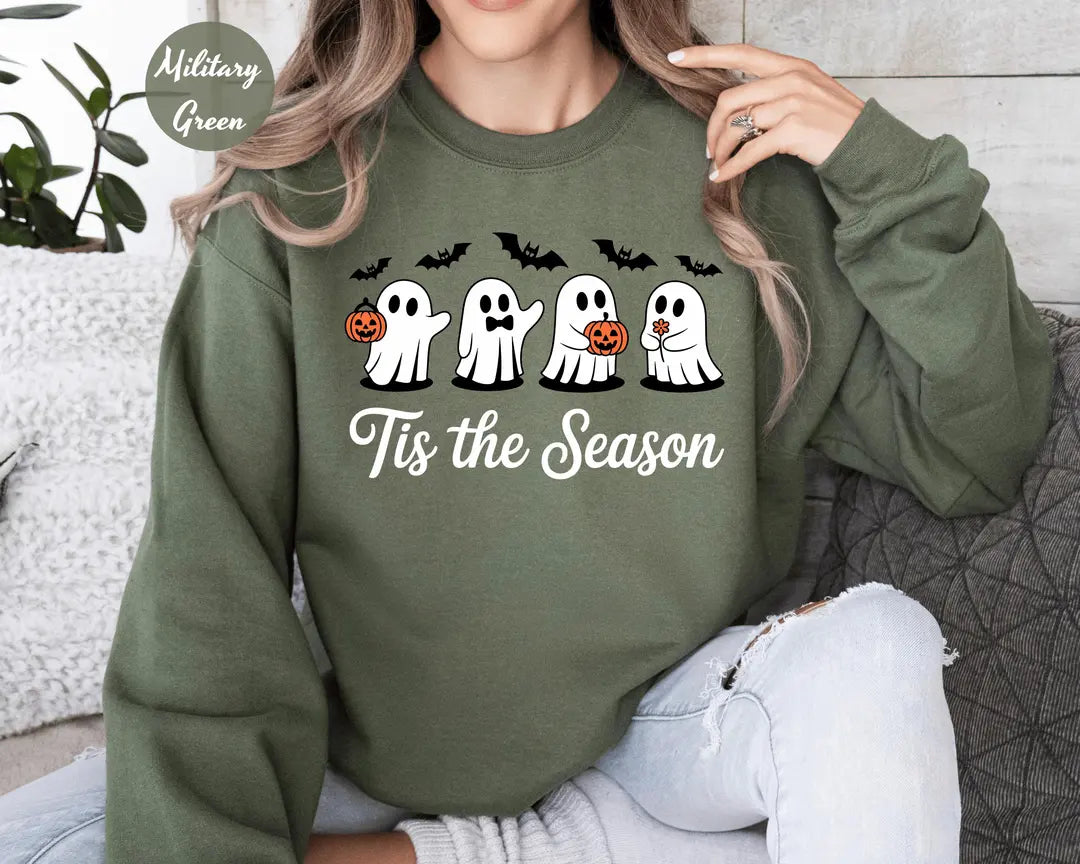 Military Green crewneck sweatshirt with printed four cute ghosts with pumpkins and bats above the words tis the season, worn by a model.