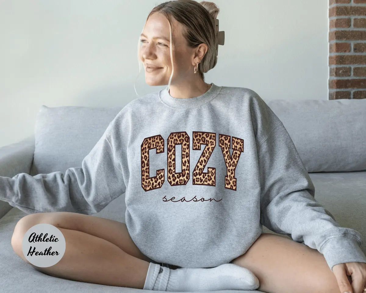 Athletic Heather crewneck sweatshirt with bold leopard print cozy lettering above the script words season, worn by a model.