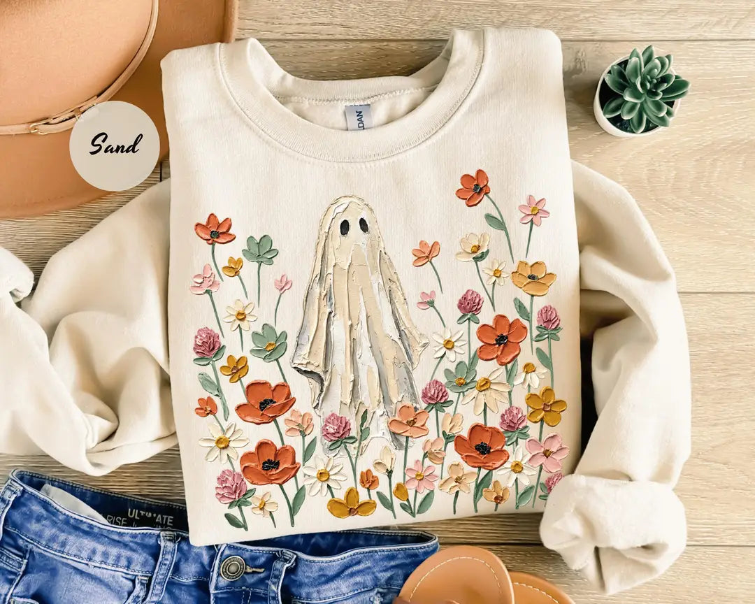 Sand crewneck sweatshirt with printed a ghost standing in a field of autumn wildflowers, flat lay view.
