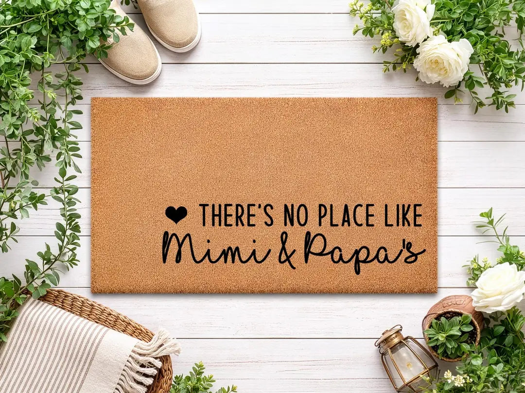 Rectangular coir doormat with a There's No Place Like Mimi and Papa's message on white wood boards with greenery, white roses, and a woven basket