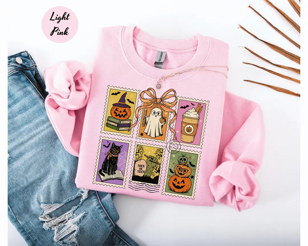 Light Pink crewneck sweatshirt with six vintage postage-style stamps with a ghost, black cat, pumpkins and a coffee cup, flat lay view.