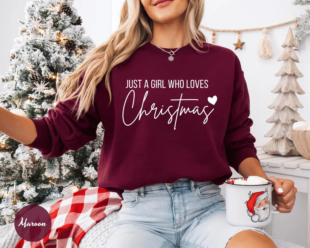 Maroon crewneck sweatshirt with script lettering that reads just a girl who loves Christmas with a small heart, worn by a model.