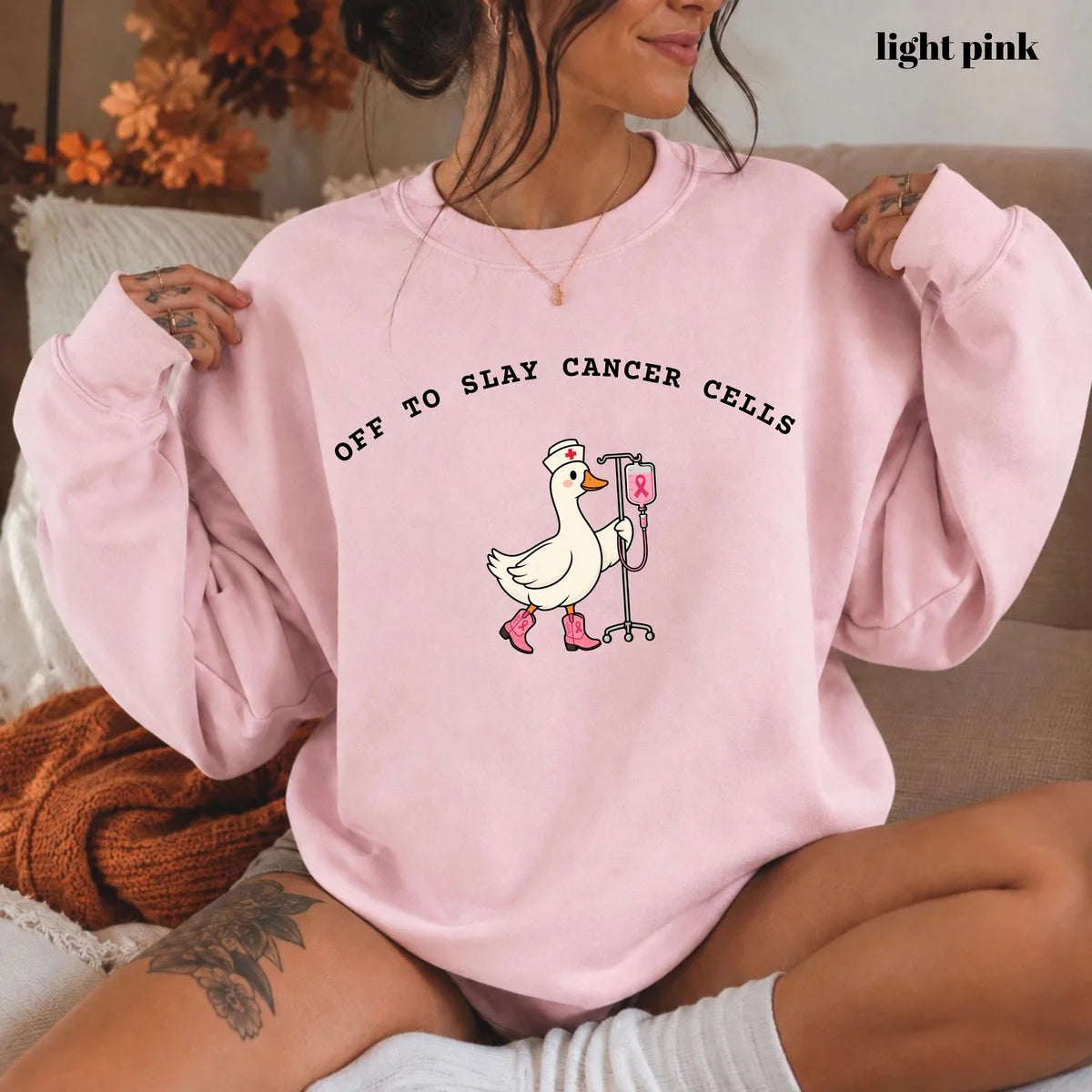 Light Pink crewneck sweatshirt with printed a nurse goose in pink boots with an IV pole and the words off to slay cancer cells, worn by a model.