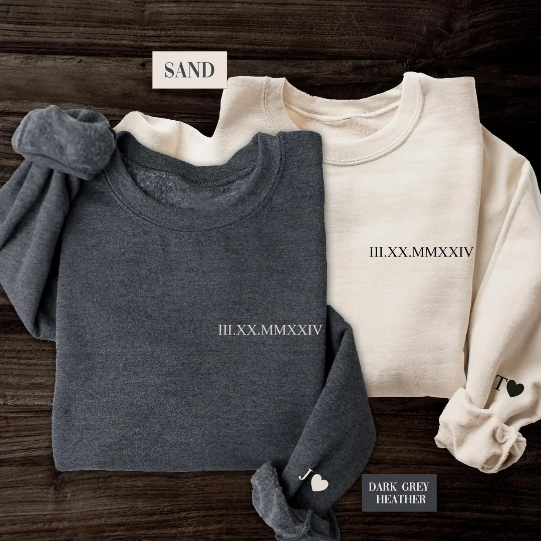 Crewneck sweatshirts in two colors showing a custom date in Roman numerals on the chest and an initial with a heart on the cuff.